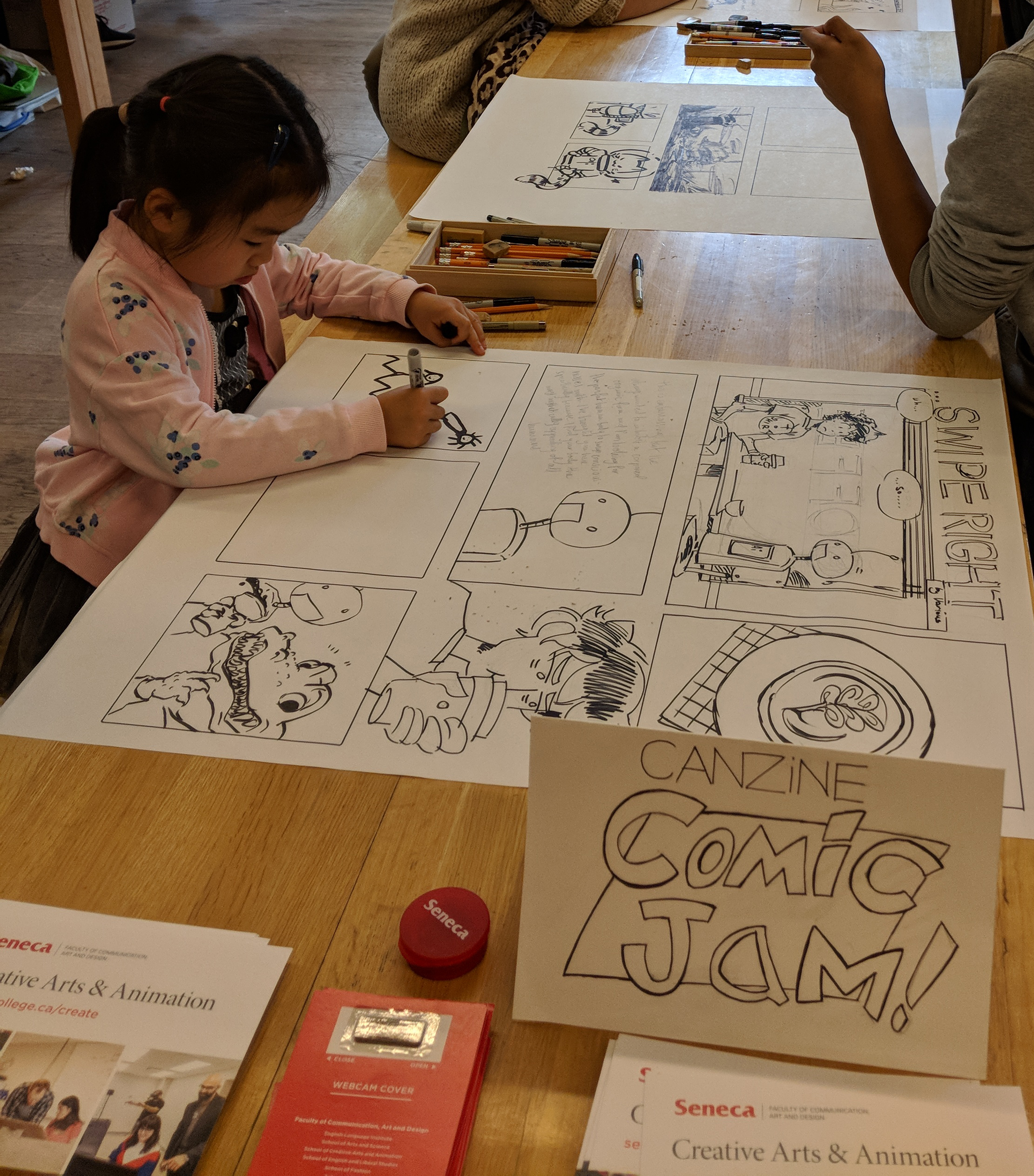 A little girl aged 4 or 5 draws one of the panels for the comic jam. The comic is about a young man who is on a first date with a robot.