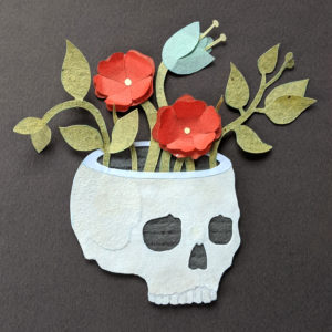 Flowers and leaves growing out of a skull. Everything is made out of paper cut-outs and layered on a grey background.