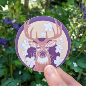 Round sticker with flowers and a deer. There is a yellow crescent moon behind the deer and flowers.